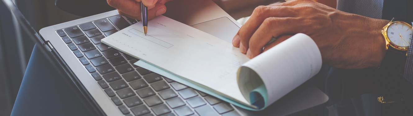 man writing out a check with a laptop in thebackground