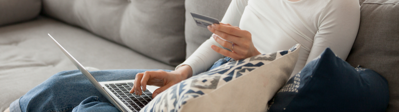 Image of woman on couch typing credit card number into computer.